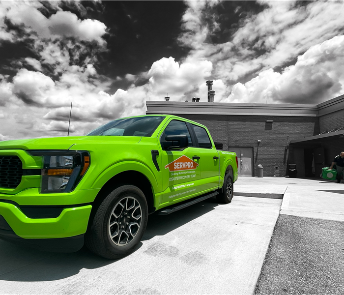 Black and White photo of the outside of a hospital with a bright green SERVPRO truck out front. 